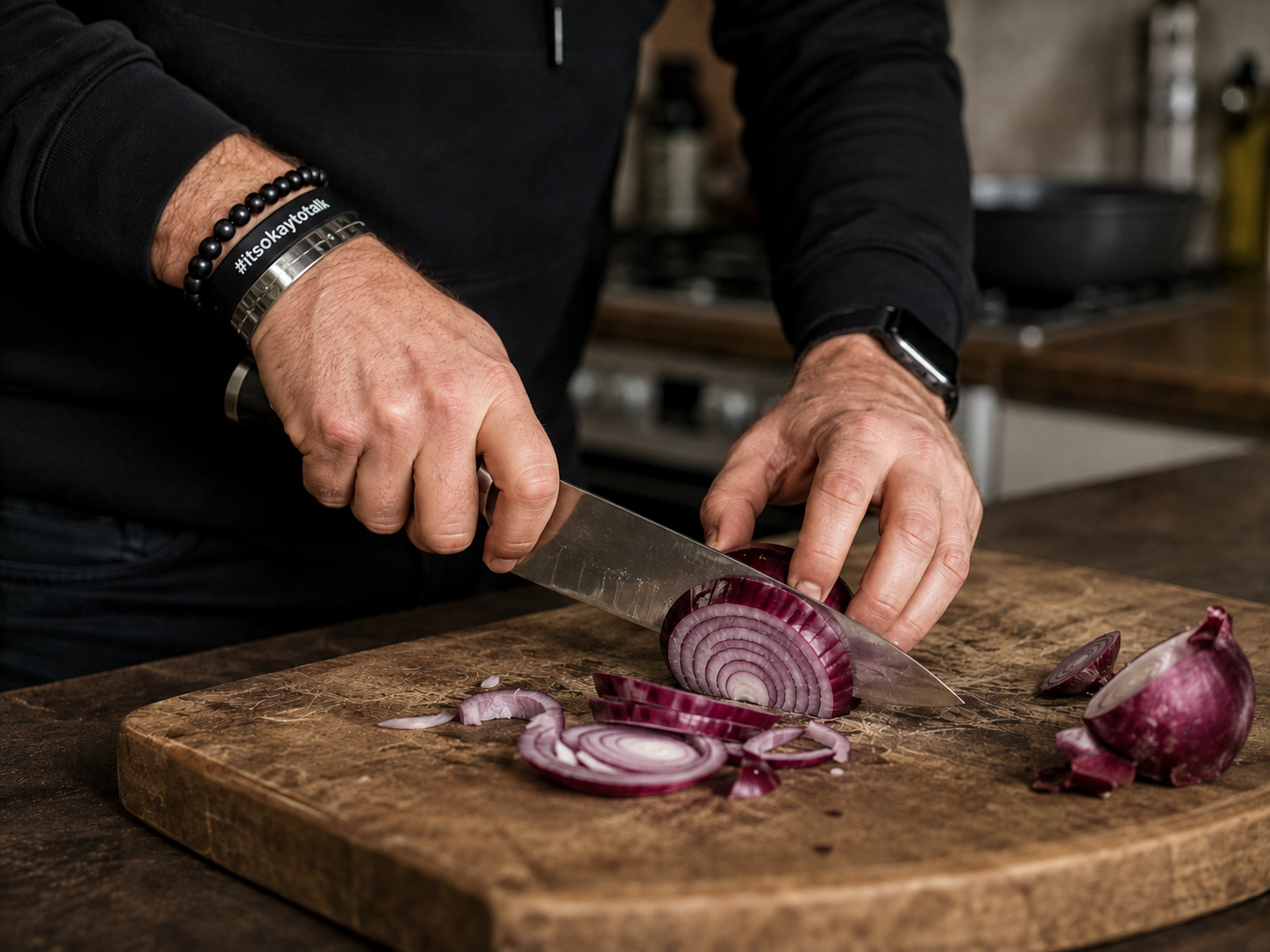 Chris Hibbert's hands slicing a red onion on a worn wooden board in a home kitchen.