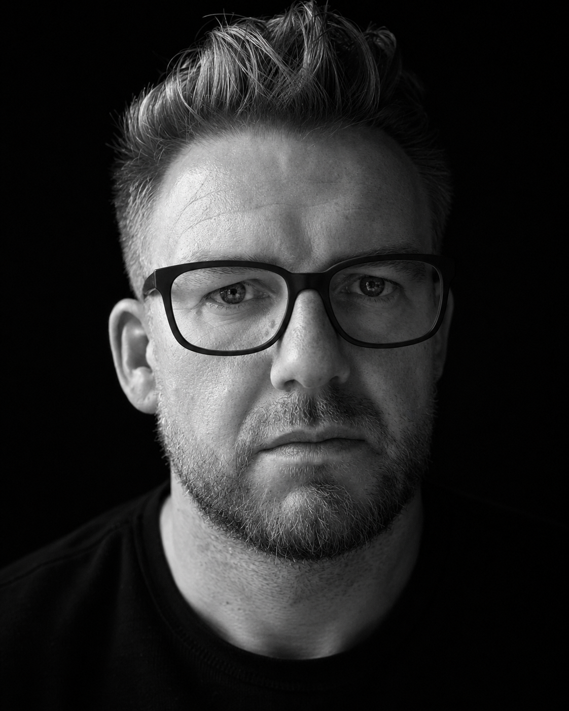 Black and white close portrait of Chris Hibbert in glasses, looking directly at camera.